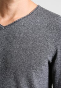 Szary sweter z dekoltem w serek wykonany z miękkiego dzianinowego materiału, z fakturą oraz subtelnymi szwami wzdłuż linii dekoltu i rękawów.