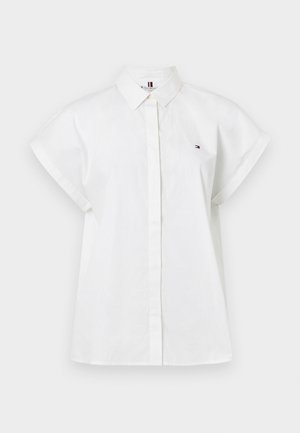 Chemise blanche à manches courtes avec un bouton sur le devant, un col et un petit logo sur la poitrine gauche. Fabriquée en tissu léger.