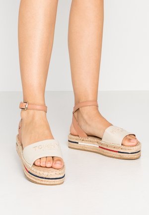 Beige espadrillesandaler med lærredsoverdel, læderankelrem, jutesål og røde, hvide og blå stribede detaljer.