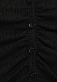 Černý pletený kardigan s plisovanými detaily a šesti černými knoflíky vpředu, představující texturovaný žebrovaný vzor.