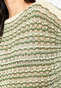 Stickad tröja med randigt mönster i gröna och beige nyanser. Lätt, öppen vävstruktur med lös, avslappnad passform och ribbad halsringning.