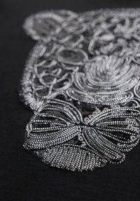 Gros plan d'un motif floral détaillé en perles argentées et sequins sur tissu noir.