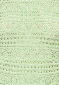 Tissu en crochet vert clair présentant des motifs complexes et des textures variées, avec des sections en maille ouverte et des rangées solides créant un effet de couches.