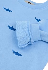 Felpa azzurra con ricamo di squalo blu scuro. Presenta polsini a coste e un collo tondo, realizzata in un tessuto a maglia testurizzato.