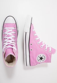 Růžové vysoké tenisky vyrobené z plátna s bílými tkaničkami, gumovou špičkou a černými akcenty. Na boku mají kruhové logo.