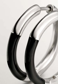 Pendientes de aro plateados y negros con un diseño tubular elegante, con metal pulido y acentos brillantes. Textura de superficie lisa.