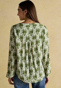 Zaļš ziedu raksts gariem piedurknēm blūze ar savelku aizmuguri, balta pamatkrāsa, mīksta auduma un izliekta apakšmalā.