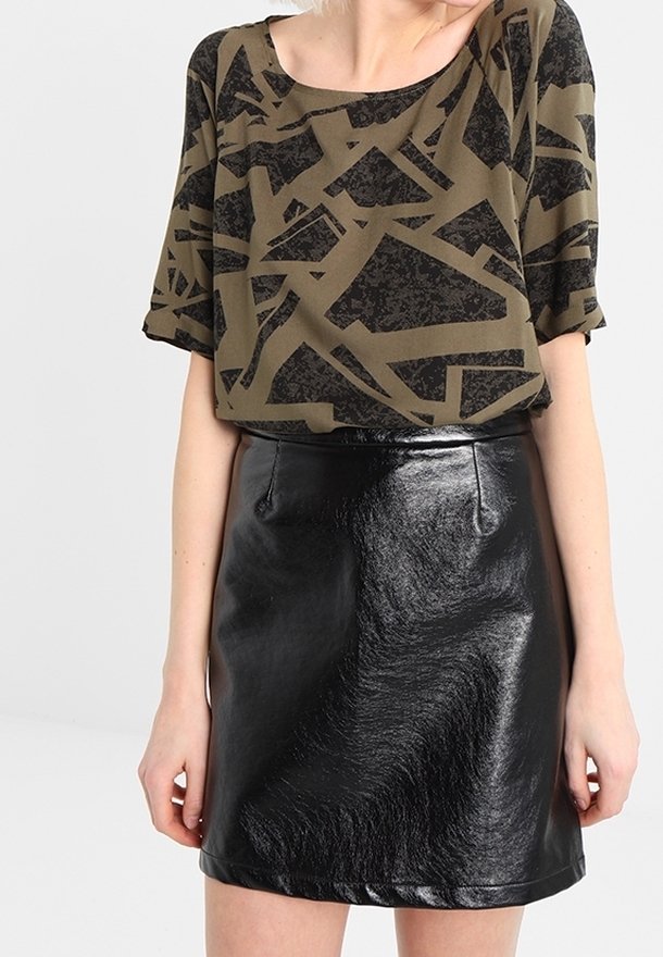 Femme portant un haut à manches courtes à motif abstrait vert olive et noir avec une mini-jupe en cuir noir brillant.