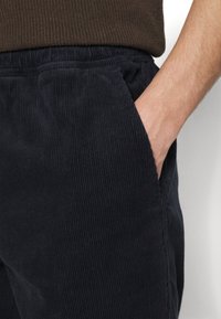 Námořnické modré kordové kalhoty s vertikálním ribbováním, obsahující boční kapsy a elastický pas, což zajišťuje strukturovaný, pohodlný střih.