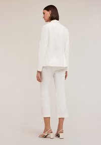 Ensemble composé d'un blazer blanc ajusté et d'un pantalon court, avec un tissu lisse, un design structuré et des sandales à talons carrés avec des brides.