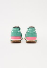 Grønne semskede joggesko med rosa og hvite detaljer, en teksturert såle og logo på hælen, som har en sporty, polstret design.