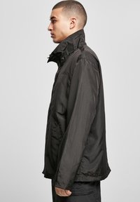 Juodas, lengvas švarkas su aukštu apykakle, pasižymintis lygiu paviršiumi ir laisvu kirpimu. Įrengti šoniniai kišeniai ir minimalūs siuvimo detalės.