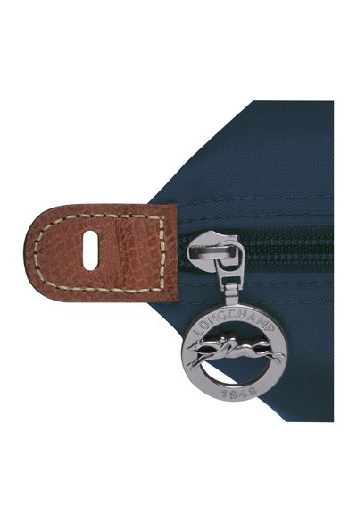 Navy nylon pouch features a brown leather tab with stitching, silver metal zipper, and a round metal pull with a logo and year.