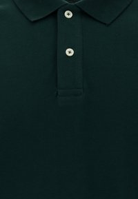 Donkergroene polo met een gestructureerde stof, een drieknoopsluiting en een klassieke kraag. Voorzien van contrasterende lichte knopen.