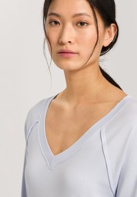 Top azzurro chiaro a scollo a V con maniche lunghe. Tessuto liscio e leggermente lucido. Presenta una vestibilità rilassata e dettagli di cucitura discreti lungo lo scollo.