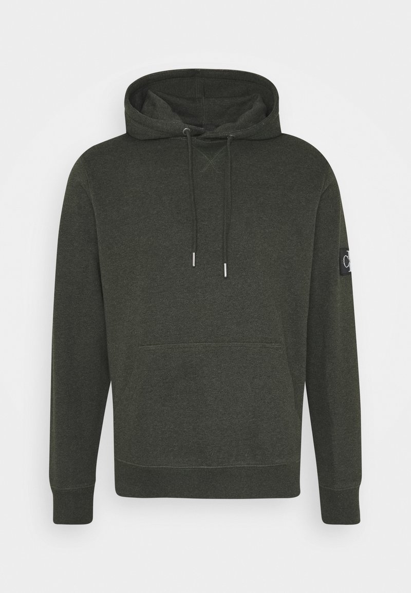 Sweat à capuche vert foncé avec poche frontale, cordons, poignets côtelés et petit patch logo sur la manche gauche.