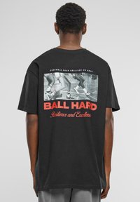Sort bomulds t-shirt med et grafisk print, der viser sneakers og rød tekst "BALL HARD Resilience and Excellence" på ryggen. Korte ærmer.