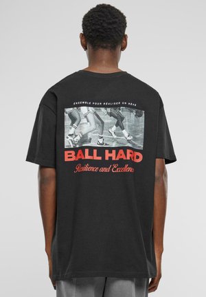 Sort bomulds t-shirt med et grafisk print, der viser sneakers og rød tekst "BALL HARD Resilience and Excellence" på ryggen. Korte ærmer.