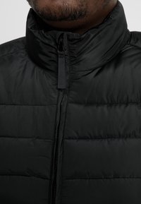 Czarna puchowa kurtka z wysokim kołnierzem, z poziomymi pikowanymi sekcjami, przednim zamkiem błyskawicznym i matową, gładką teksturą.