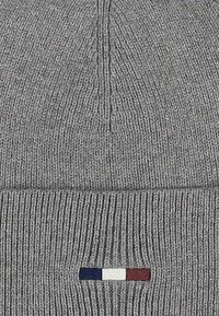 Gray knit beanie with a ribbed texture, featuring a horizontal accent stripe with blue, white, and burgundy colors near the bottom.