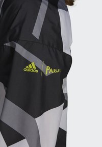 Adidas Parley jakke med et geometrisk mønster i sort, grå og hvid samt klare gule logoaccenter. Letvægts-, vandafvisende materiale.