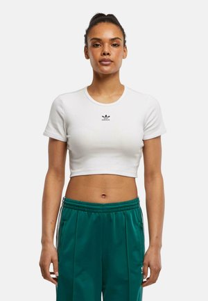 Vit kortärmad crop top i ribbat tyg, med en liten svart "adidas"-logotyp på bröstet. Bärs med gröna träningsbyxor.