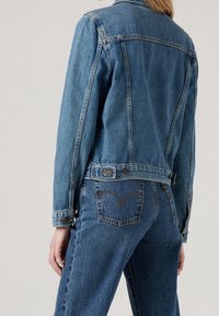 Denimjacka i ljusblått med en klassisk design, med knäppte ärmslut och en cinchad midja. Distinkt sömnad på bakfickorna.