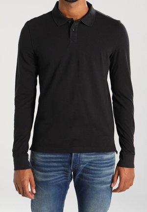 Polo noir à manches longues avec col, doté d'une patte de boutonnage à trois boutons, fabriqué dans un tissu doux. Associé à un jean en denim bleu.