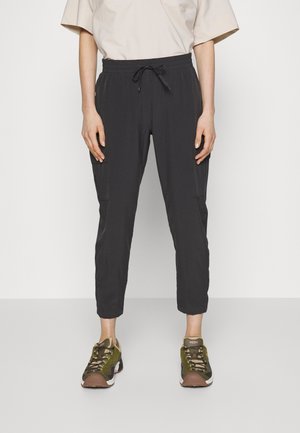 Pantalones oscuros de corte holgado con cintura elástica y cordón. Incluyen bolsillos cargo a los lados. Combinados con zapatillas verdes y marrones.