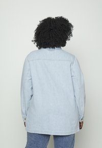 Jasnoniebieska denimowa kurtka z długimi rękawami, luźnym krojem i zapinanymi mankietami. Prosty design z klasycznym kołnierzem, bez wyróżniających się wzorów.
