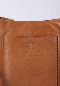 Brown leather handbag with a textured surface, visible stitching, and a pocket featuring an embossed logo at the top.