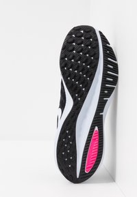 Sole di scarpa sportiva in bianco e nero con gomma testurizzata in un motivo esagonale, caratterizzata da un'etichetta Zoom rosa e una suola intermedia bianca.