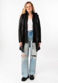 Zwarte leren lange jas met een capuchon, ritssluiting aan de voorkant en gewatteerde voering, gecombineerd met lichtblauwe gescheurde jeans en zwarte plateau schoenen.