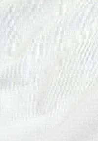 Gros plan sur un tissu blanc doux avec une texture en maille côtelée verticale fine et de légers plis.