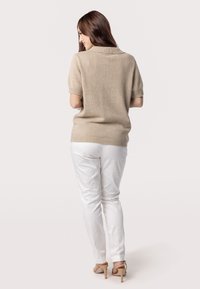 Beige trui met korte mouwen en een kraag, gecombineerd met witte, strakke broeken en beige hoge hakken, gezien vanaf de achterkant.