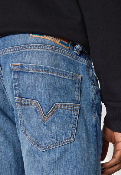 Gros plan sur une personne portant un jean en denim bleu clair avec une poche arrière cousue et un haut à manches longues noir.