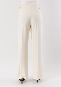 Pantaloni a gamba larga in tessuto crema, caratterizzati da una superficie liscia, vita alta e pieghe sottili con una silhouette pulita e sartoriale.