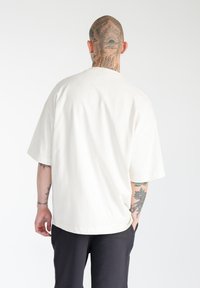 T-shirt oversize crema, maniche corte, colletto rotondo, materiale in cotone morbido. Design semplice senza motivi o grafiche visibili.