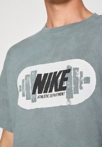 Grå bomulds T-shirt med et stort sort-hvidt "NIKE" logo samt teksten "ATHLETIC DEPARTMENT", korte ærmer og rund halsudskæring.