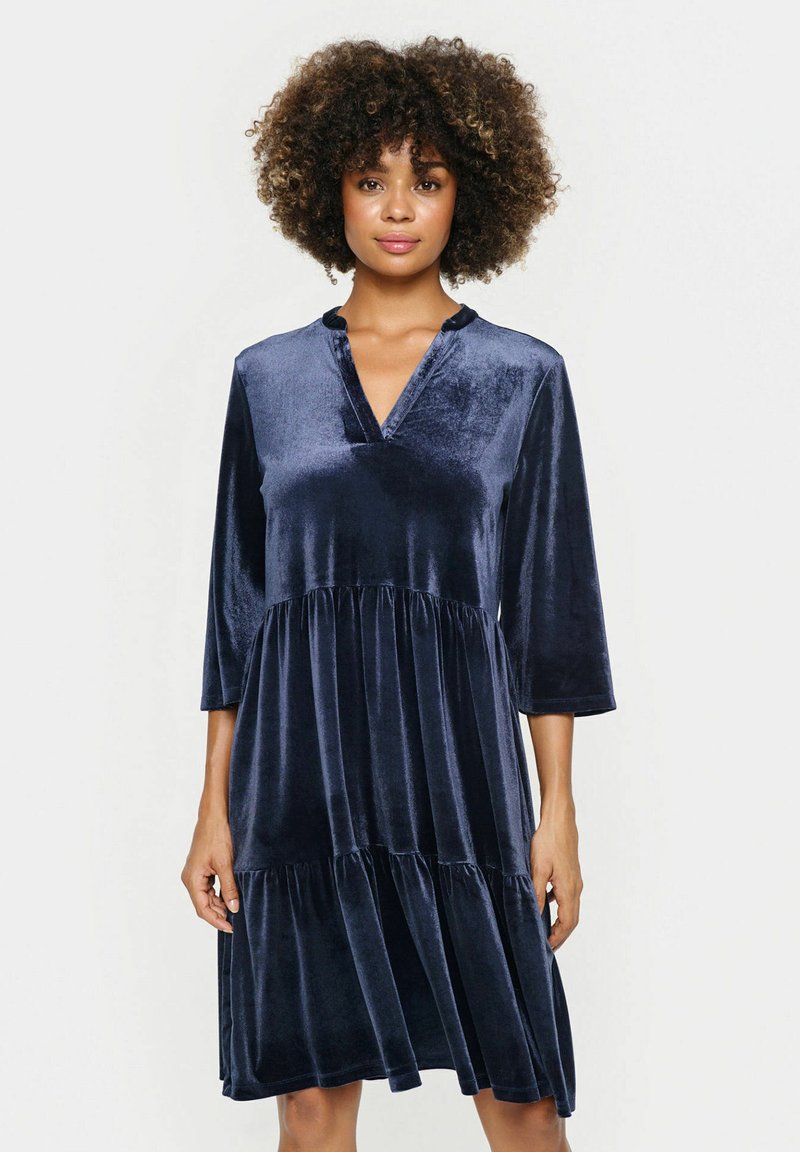 Rochie din catifea bleumarin, cu decolteu în V, mâneci trei sferturi și design cu fuste suprapuse; textură netedă și strălucire subtilă.