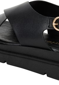 Sandal din piele neagră, cu o curea lată și un detaliu circular din metal auriu. Prezintă o talpă texturată de culoare neagră și o talpă conturată pentru suport.