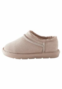 Pantoufle beige avec un extérieur doux en suède, forme arrondie et accents cousus le long de l'ouverture et des côtés. Semelle en caoutchouc.