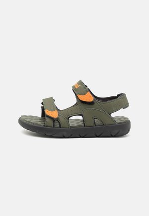 Grøn og sort sandal med åben tå, orange velcroremme og en tyk polstret sål, vist fra siden på hvid baggrund.