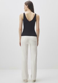 Top nero senza maniche con scollo a V profondo sul retro, abbinato a pantaloni bianchi a gamba larga e sneakers chiare, caratterizzato da un design e una struttura minimalisti.