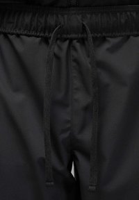 Black jogger pants featuring a smooth, matte texture, elastic waistband with external drawstrings, and no visible patterns or accents.