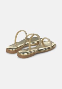 Gouden platte sandalen met twee dunne riempjes versierd met strass. Glanzende metallic afwerking, gewatteerde binnenzool en rubberen buitenzool. Gladde textuur.