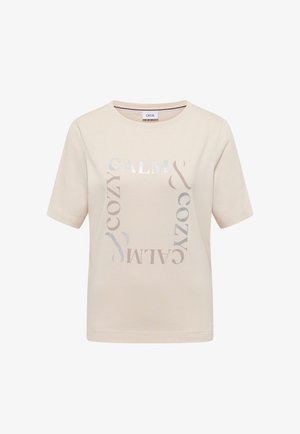 Light beige short-sleeve T-shirt in soft fabric featuring a central graphic design with the words "CALM" and "COZY" in metallic silver and grey.