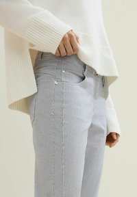 Gestreifte, hellblaue Jeans aus Denim mit tailliertem Schnitt und Vordertaschen, getragen mit einem weißen Strickpullover mit gerippten Ärmeln.