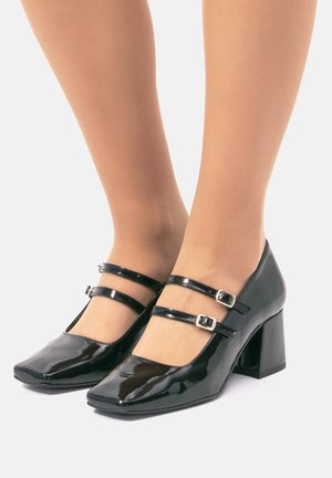 Zapatos de charol negro tipo Mary Jane con punta cuadrada, doble tira y acentos de hebilla, y diseño de tacón bloque. Acabado suave y brillante.
