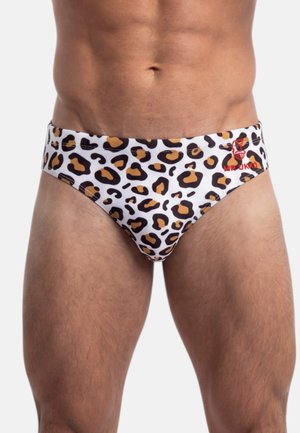 Männlicher Torso trägt weiße Badehosen mit braunem und schwarzem Leopardenmuster und einem kleinen roten Logo auf der linken Seite.